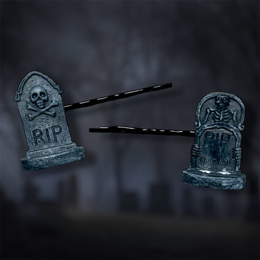 Two tombstone-shaped hair pins with 'RIP' on a dark background