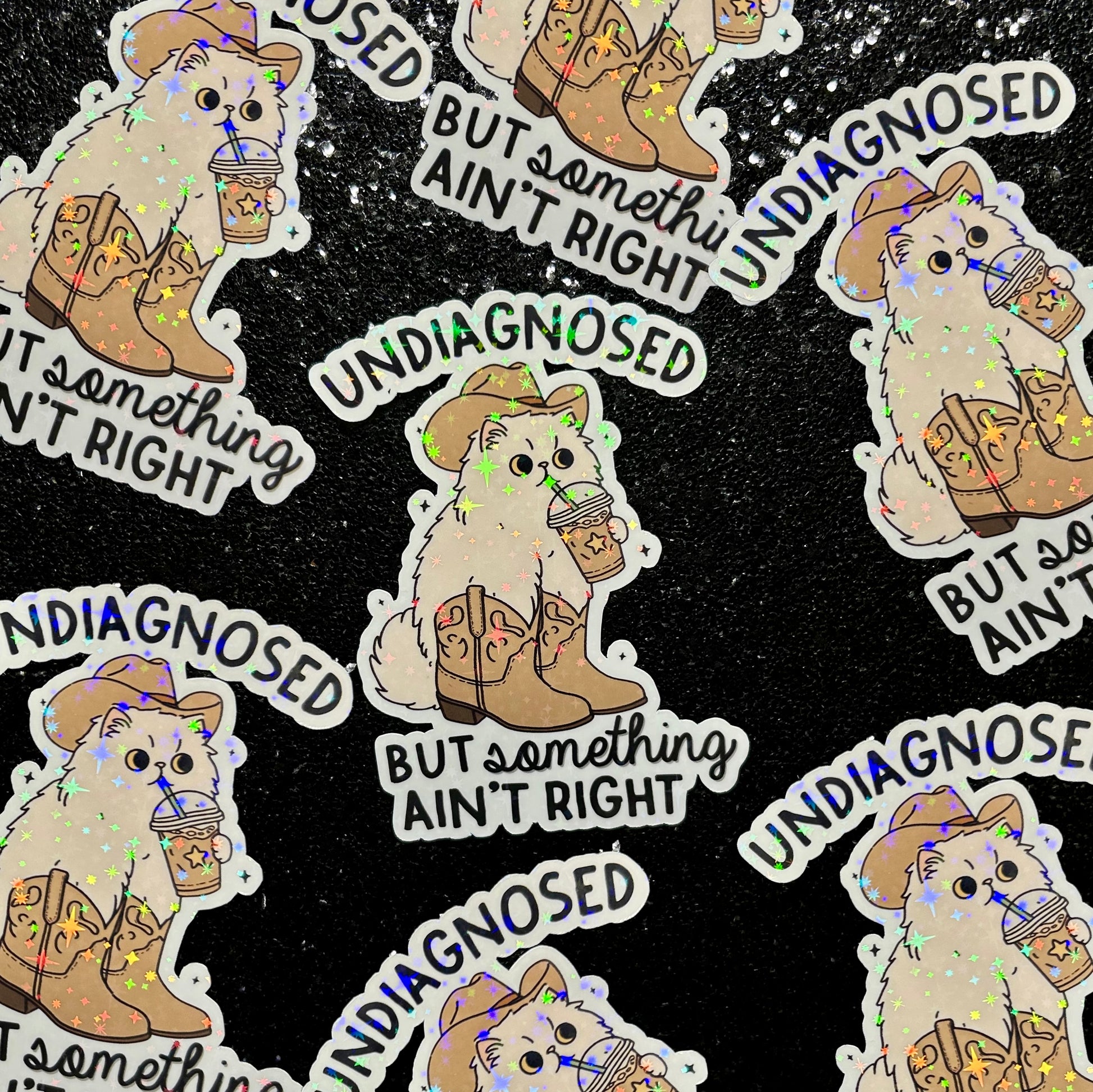 Stickers with a cartoon cat wearing a cowboy hat and boots, drinking an iced coffee, with text 'Undiagnosed but Something Ain't Right' on a black background.