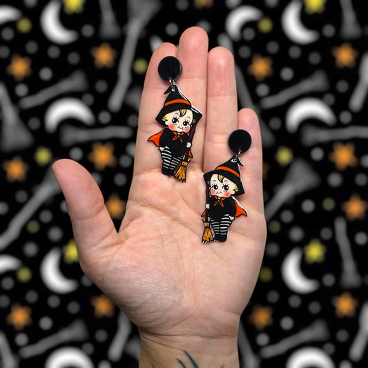 Hand holding Halloween cute witch kewpie resin earrings on a blurry background