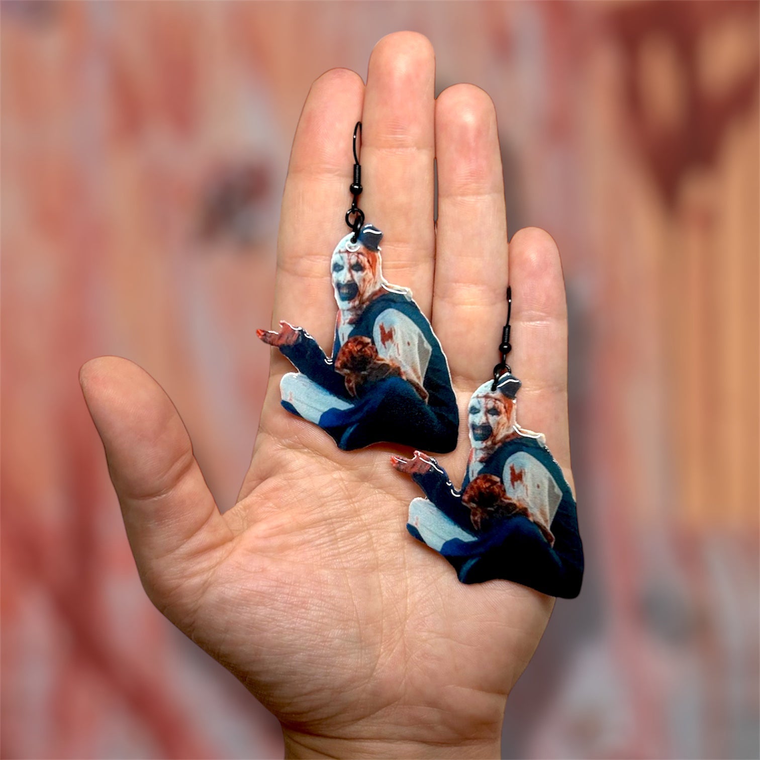 Hand holding Terrifier Art the Clown bloody outfit scary clown bedroom scene resin earrings on a blurred background