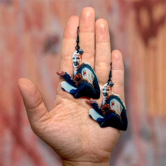 Hand holding Terrifier Art the Clown bloody outfit scary clown bedroom scene resin earrings on a blurred background