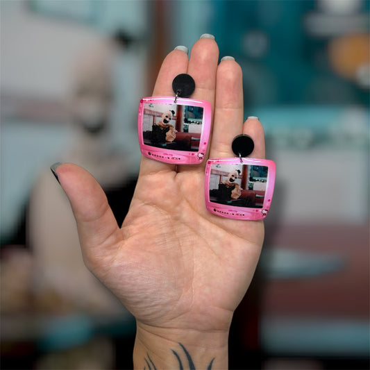 Hand holding a pair of Terrifier Art the Clown diner scene Hello Kitty TV resin dangle earrings on a blurry background