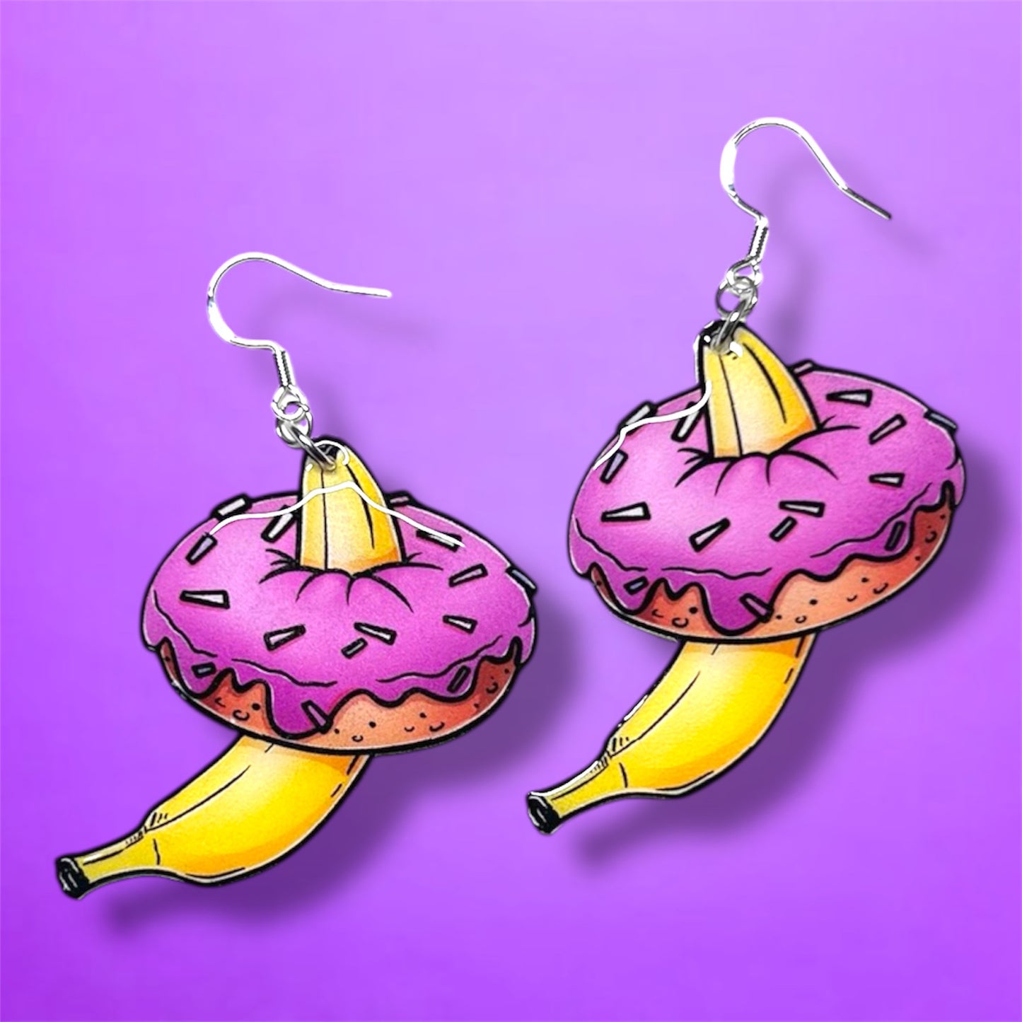 Banana inside pink sprinkle donut resin dangle earrings on a purple background