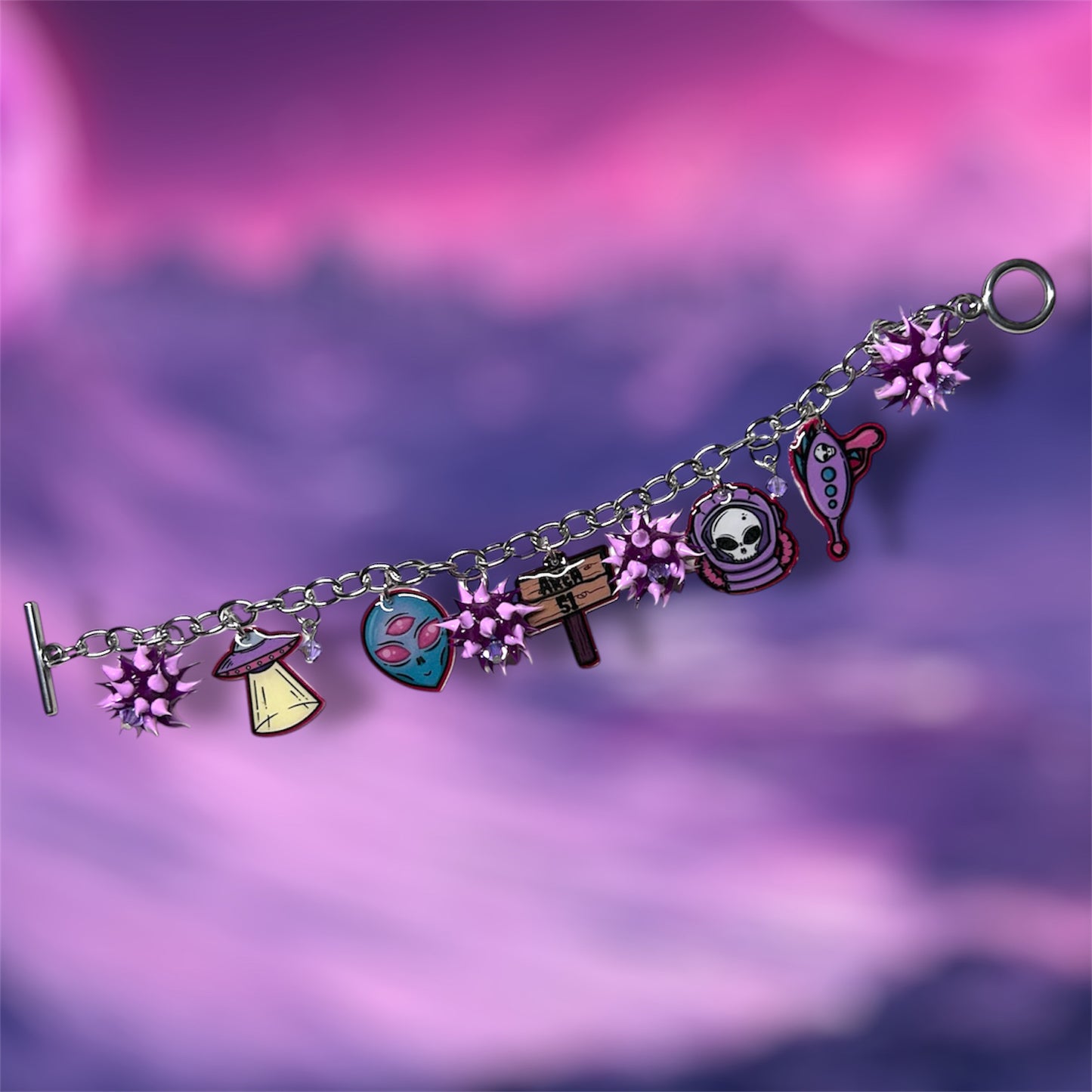 Area 51 alien charm bracelet with purple rubber spiky beads on a blurry pink and purple background