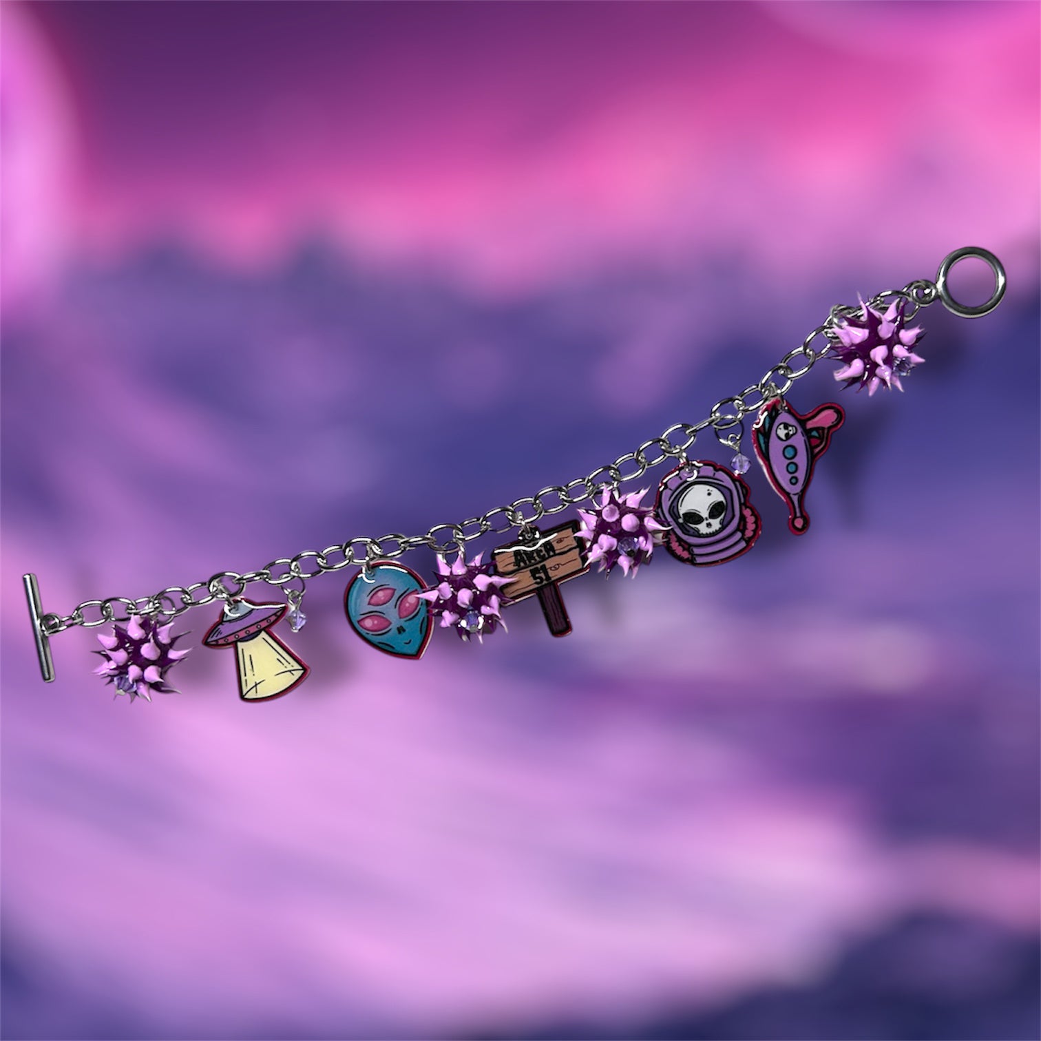 Area 51 alien charm bracelet with purple rubber spiky beads on a blurry pink and purple background