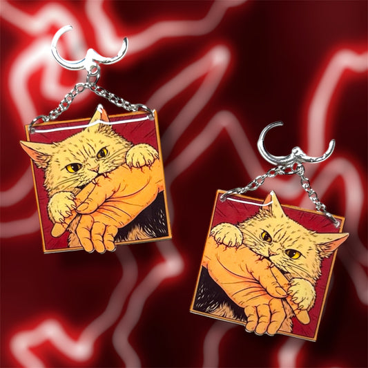 Angry cat biting hand comic book panel art resin statement earrings on a blurry red background