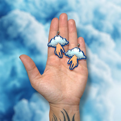 Hand holding blue cloud hand oddities and curiosities statement earrings on a blue background