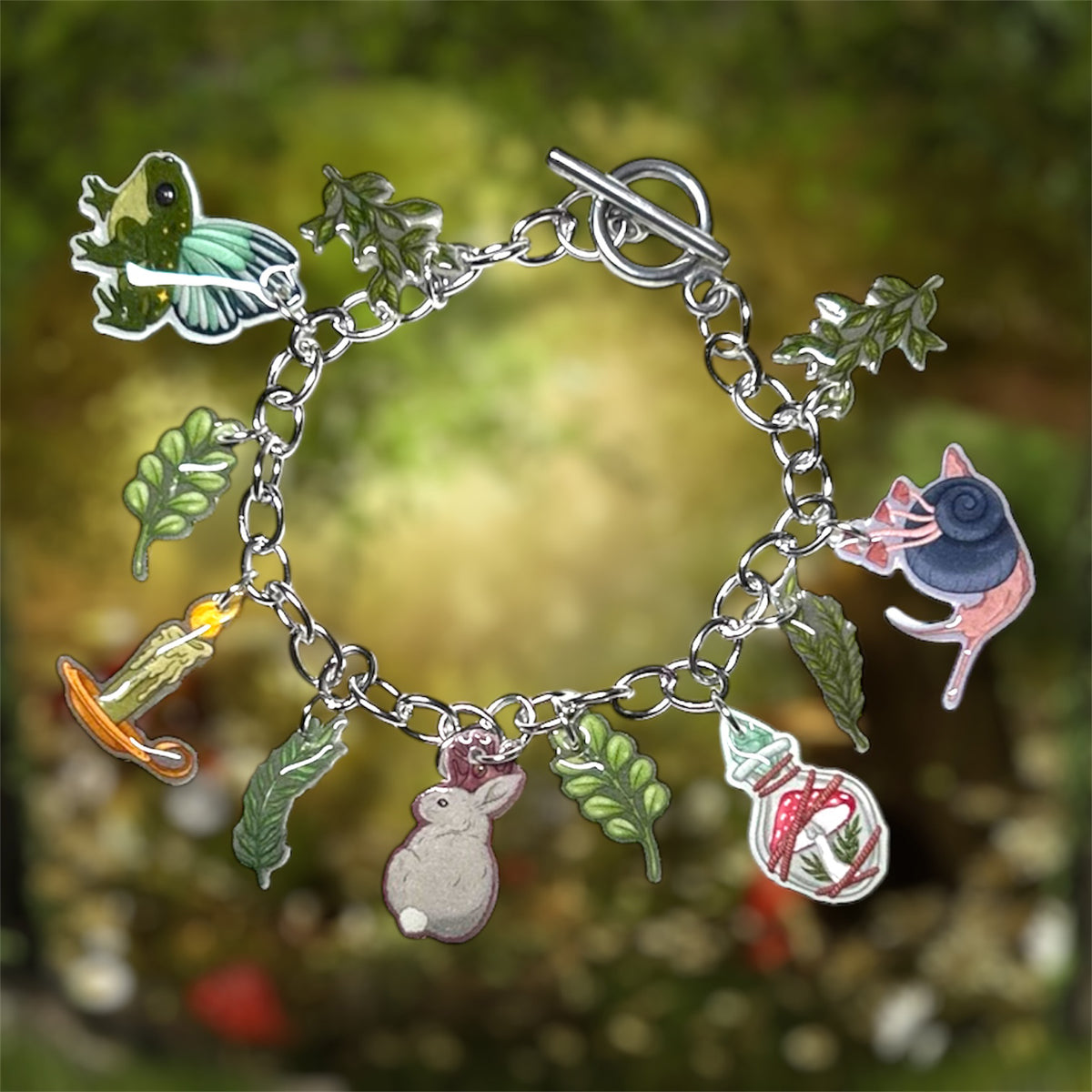 Witchy forest cottagecore charm bracelet with various charms including a frog, caterpillar, rabbit, snail, and leaves on a blurred natural background.
