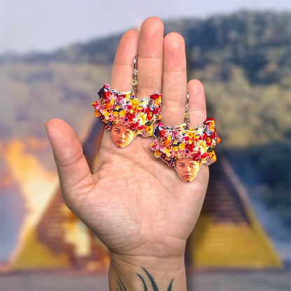 Hand holding a pair of Midsommar May Queen beaded resin statement earrings on a blurred background