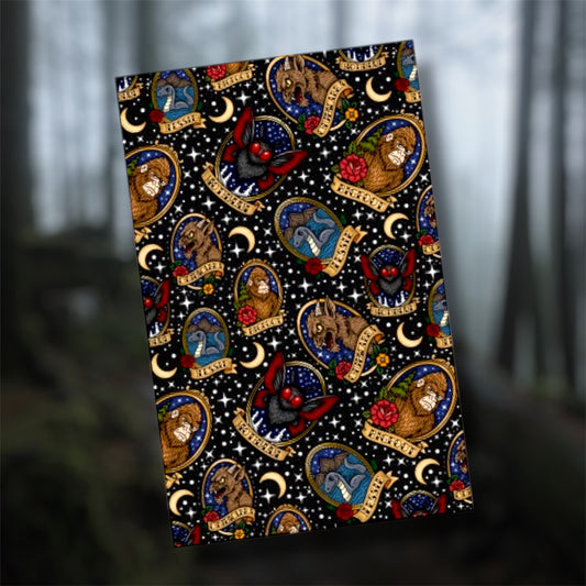 Framed cryptid art pocket notebook, featuring the Chupacabra, Mothman, Bigfoot, and the Loch Ness monster, with traditional style flowers on a blurry forest background