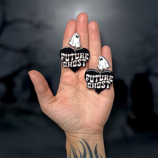 Hand holding Future Ghost heart-shaped statement earrings with sheet ghost studs on a blurry background