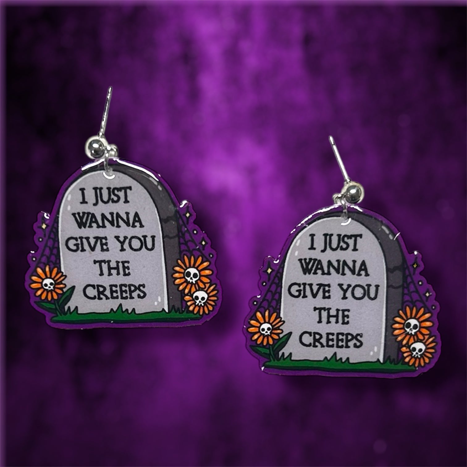 Spooky skull flower tombstone "I just wanna give you the creeps" resin statement earrings on a blurry purple and black background