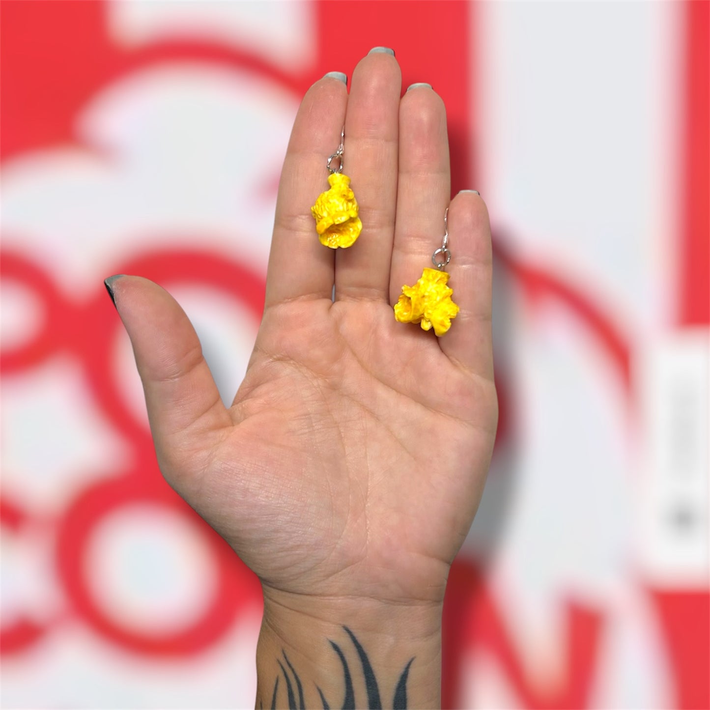 Hand holding a pair of buttered popcorn dangle earrings on a red and white popcorn bucket background