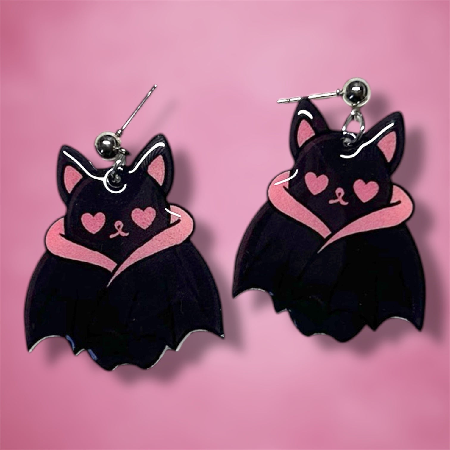 Black bat earrings with pink heart eyes on a pink background