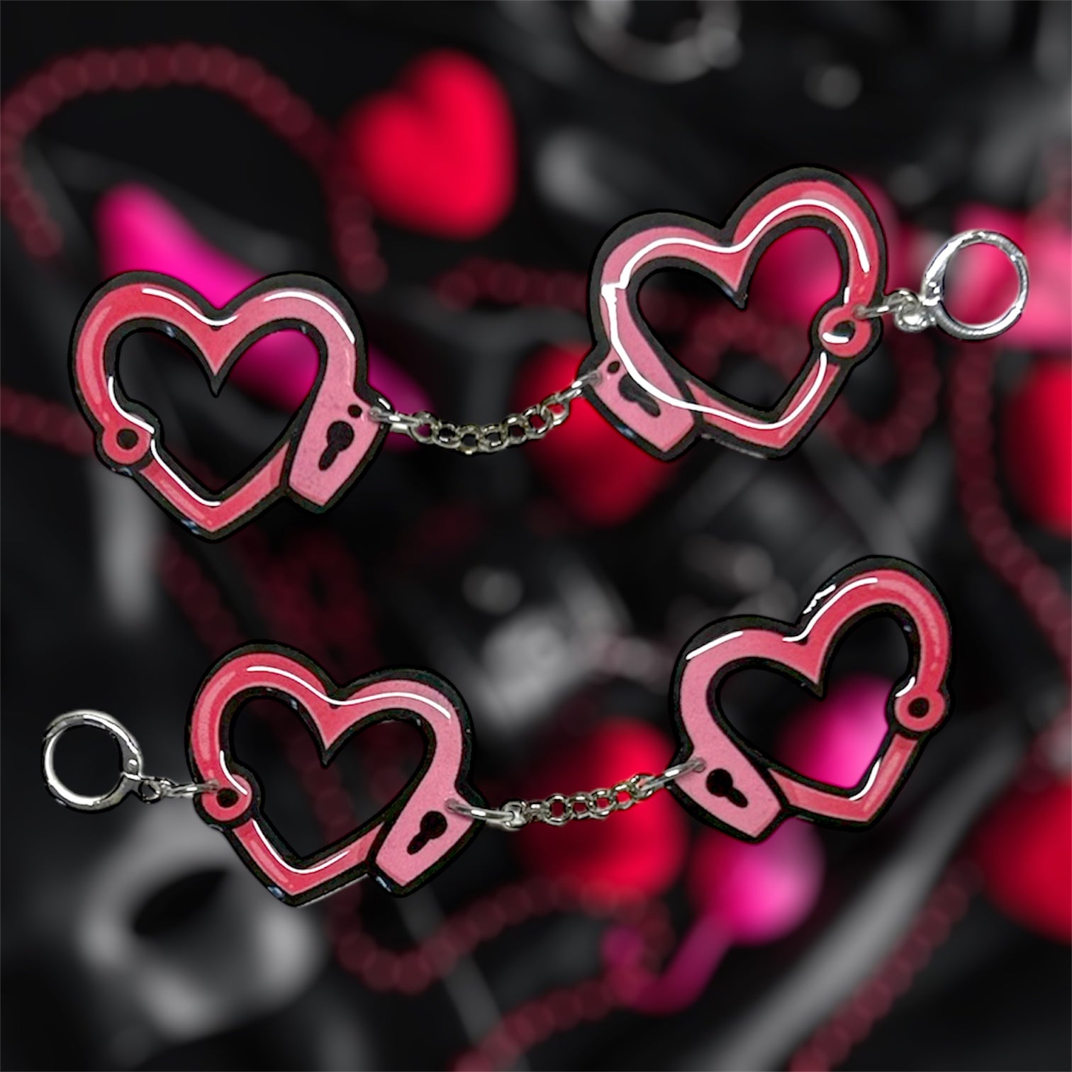 Heart-shaped pink and black handcuff dangle earrings on a blurred pink and black background
