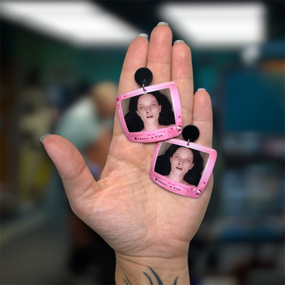 Hand holding a pair of The Autopsy of Jane Doe Hello Kitty TV resin dangle earrings on a blurry background