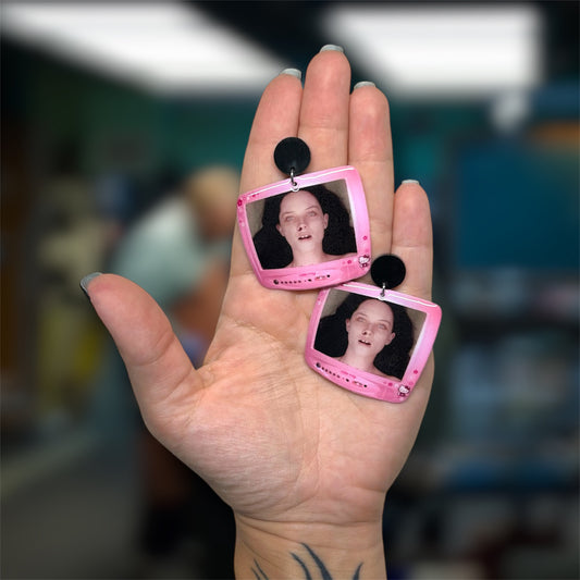 Hand holding a pair of The Autopsy of Jane Doe Hello Kitty TV resin dangle earrings on a blurry background
