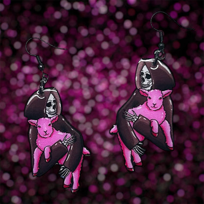 A pair of earrings of a Grim Reaper skeleton holding a pink lamb on a blurred glittery pink background.