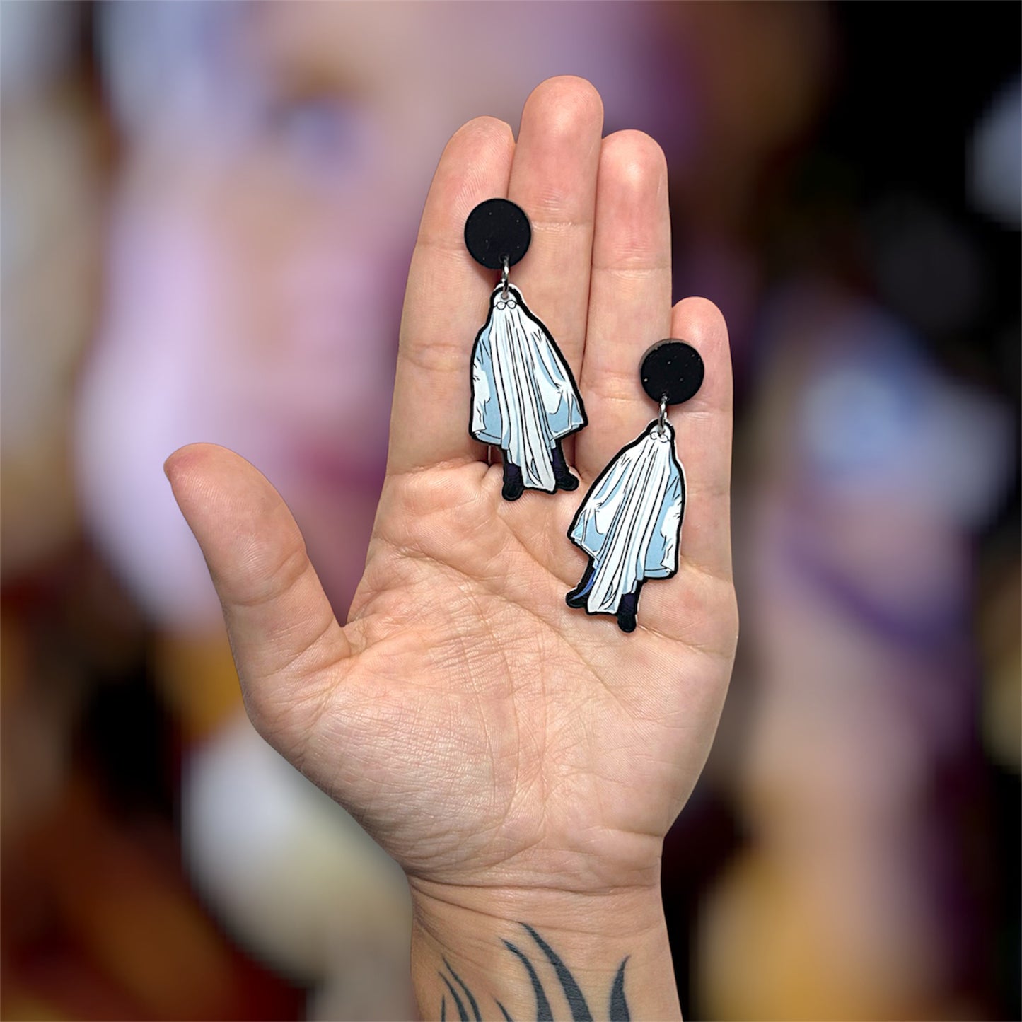 Hand holding a pair of Halloween Michael Myers sheet ghost resin dangle earrings on a blurry background