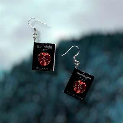 Midnight Sun miniature sparkly vampire book dangle earrings on a blurry blue background