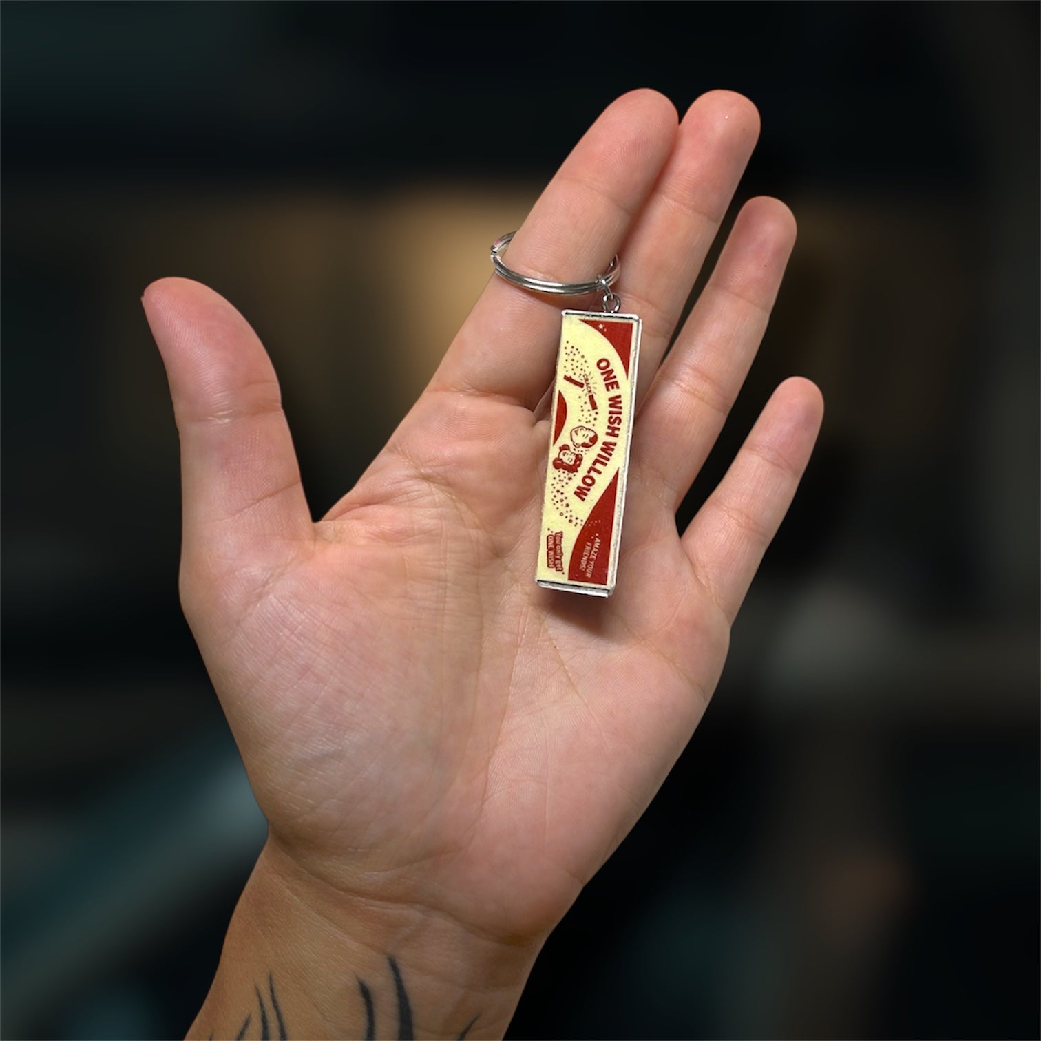 A hand holding an Obsession-inspired One Wish Willow box replica keychain on a blurry backgroud.