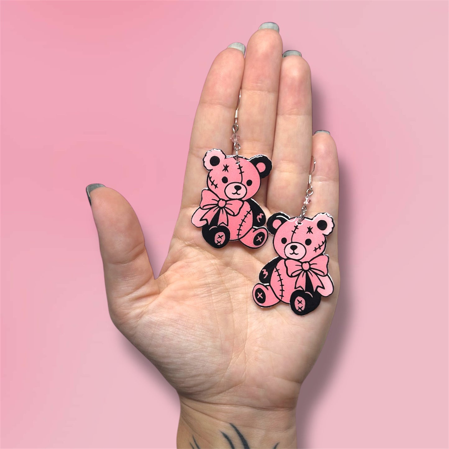 Hand holding pink and black teddy bear beaded resin statement earrings on a pink background