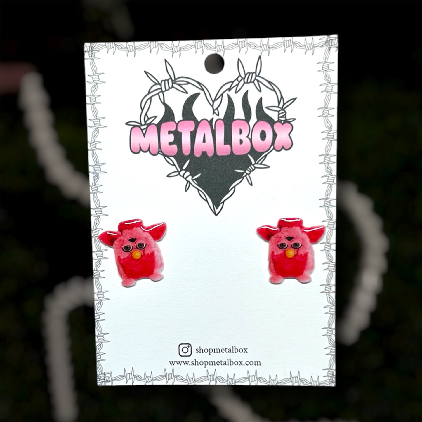 Bright pink Furby resin stud earrings on a blurry background