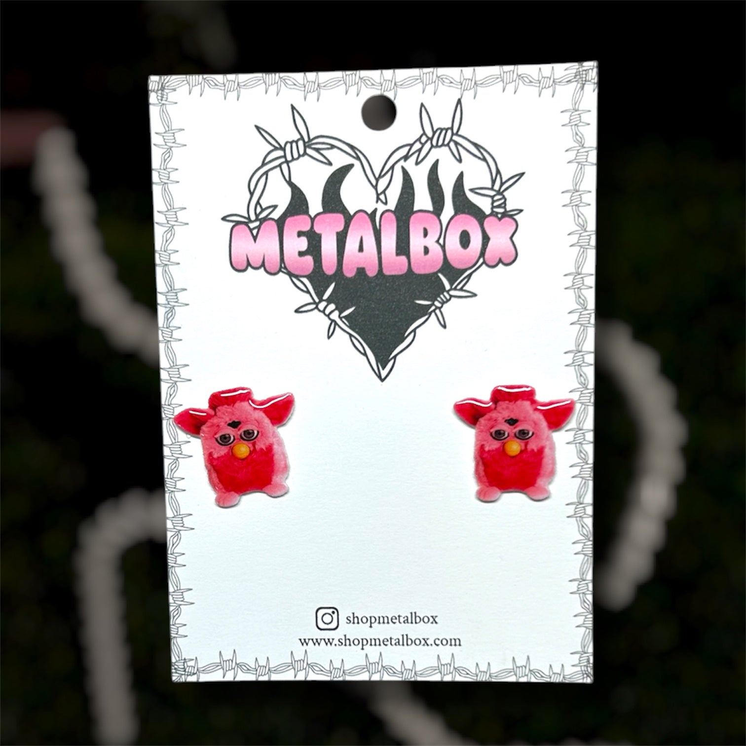 Bright pink Furby resin stud earrings on a blurry background