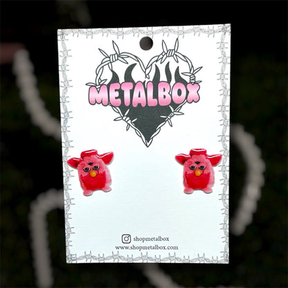 Bright pink Furby resin stud earrings on a blurry background