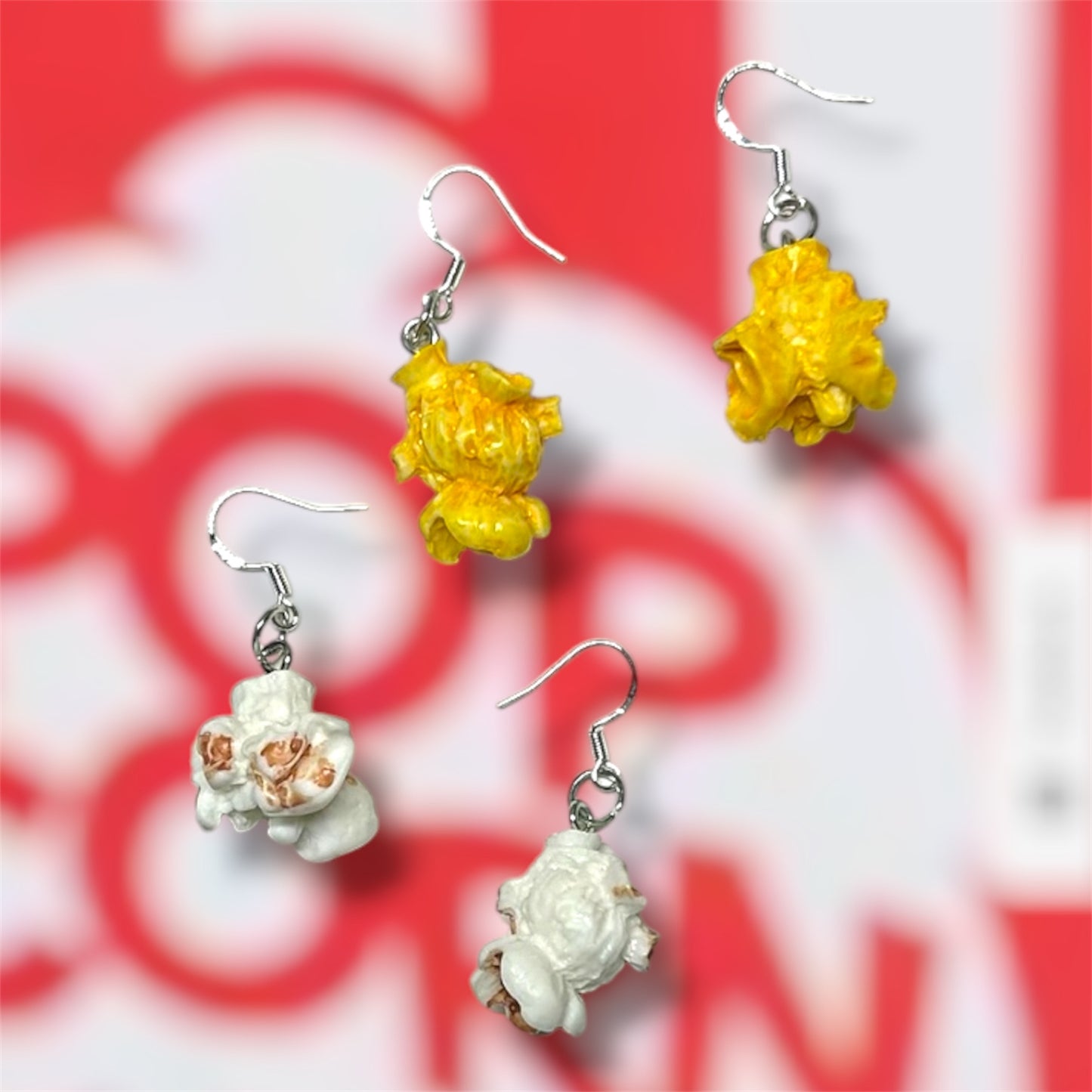 Buttered popcorn and plain popcorn dangle earrings on a red and white popcorn bucket background