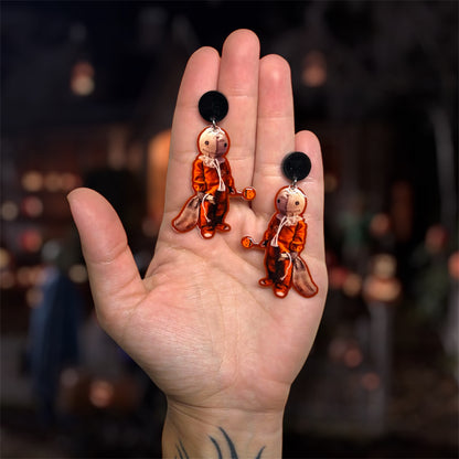 Hand holding a pair of Trick-r-Treat Sam with lollipop resin dangle earrings on a blurred background