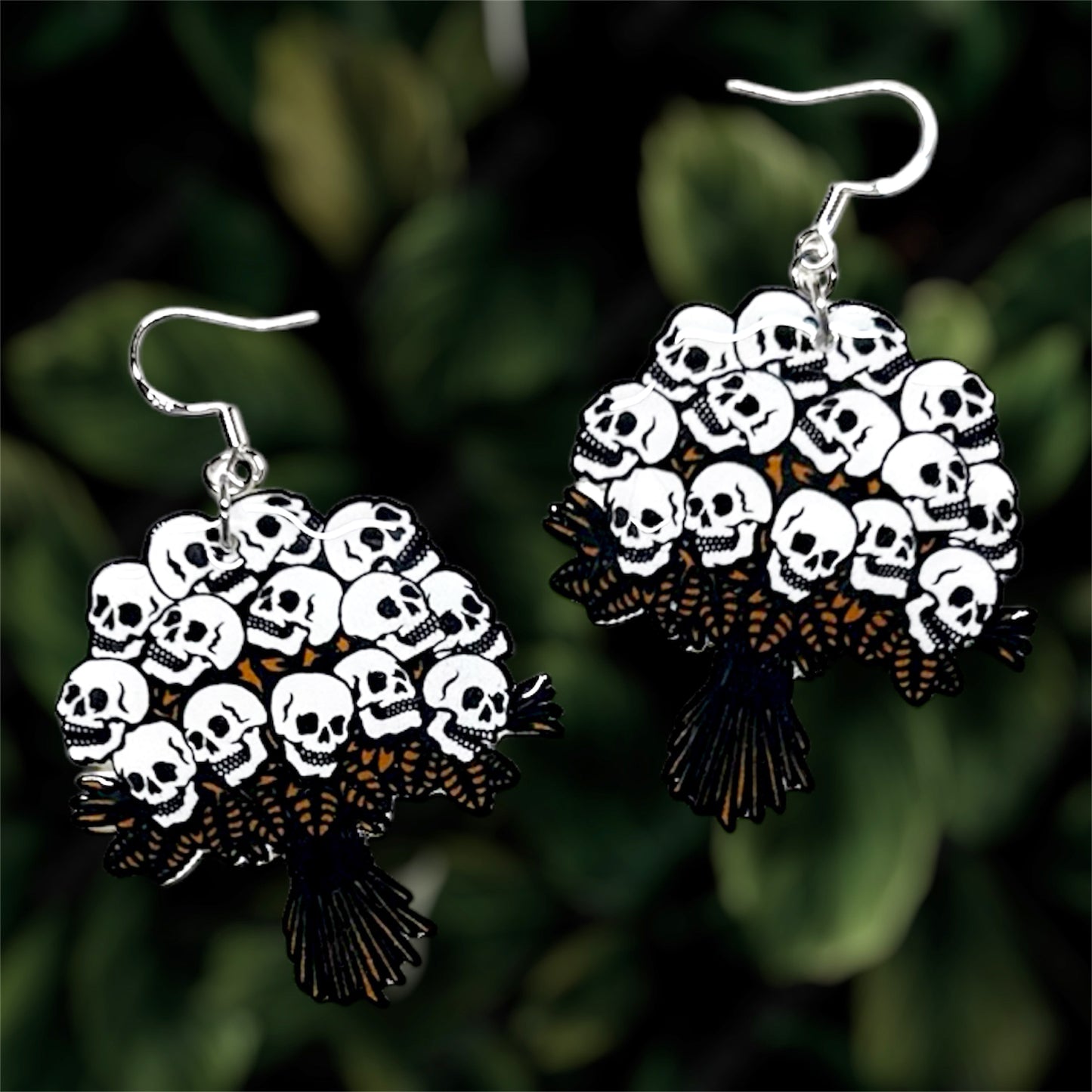 Human skull flower bouquet spooky resin dangle earrings on a leafy green blurred background