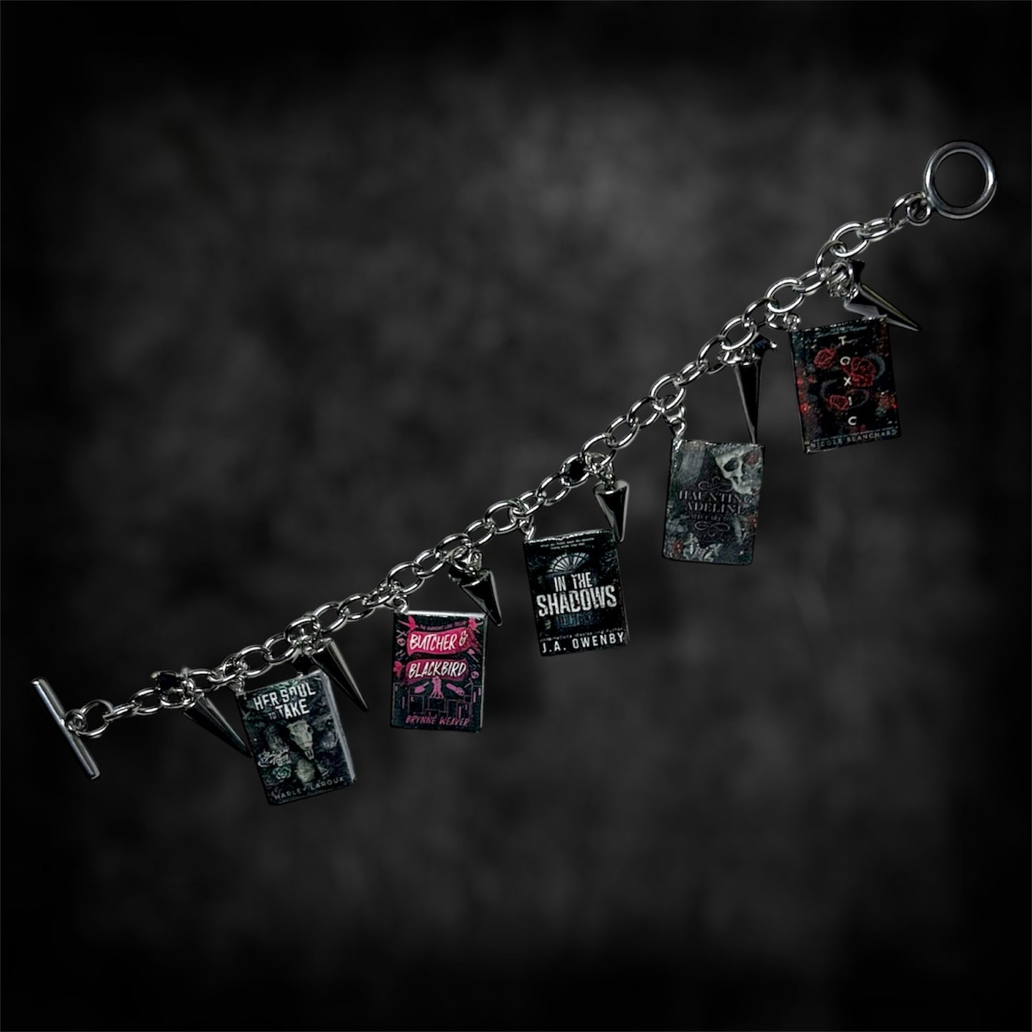 Unfastened smut book charm bracelet on a blurred black distressed background