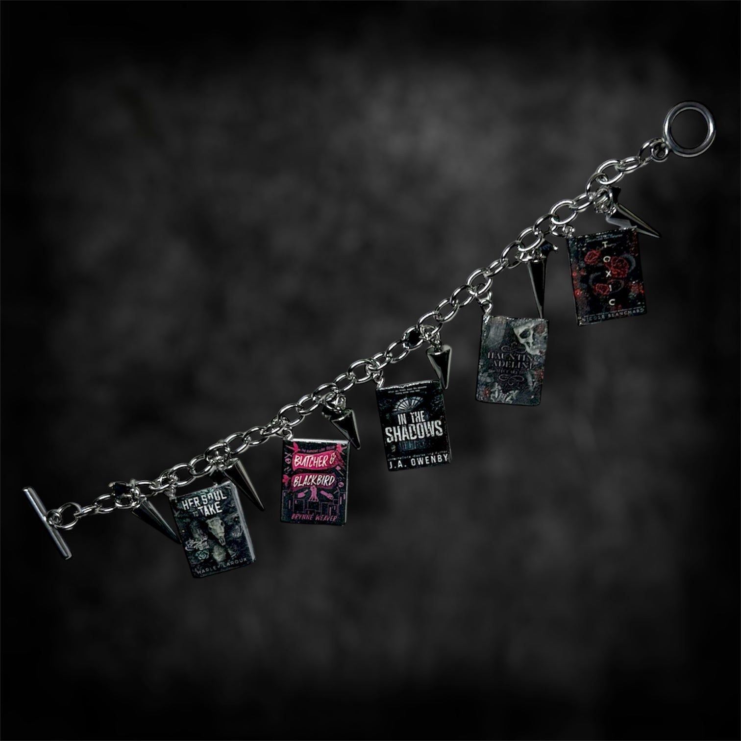 Unfastened smut book charm bracelet on a blurred black distressed background