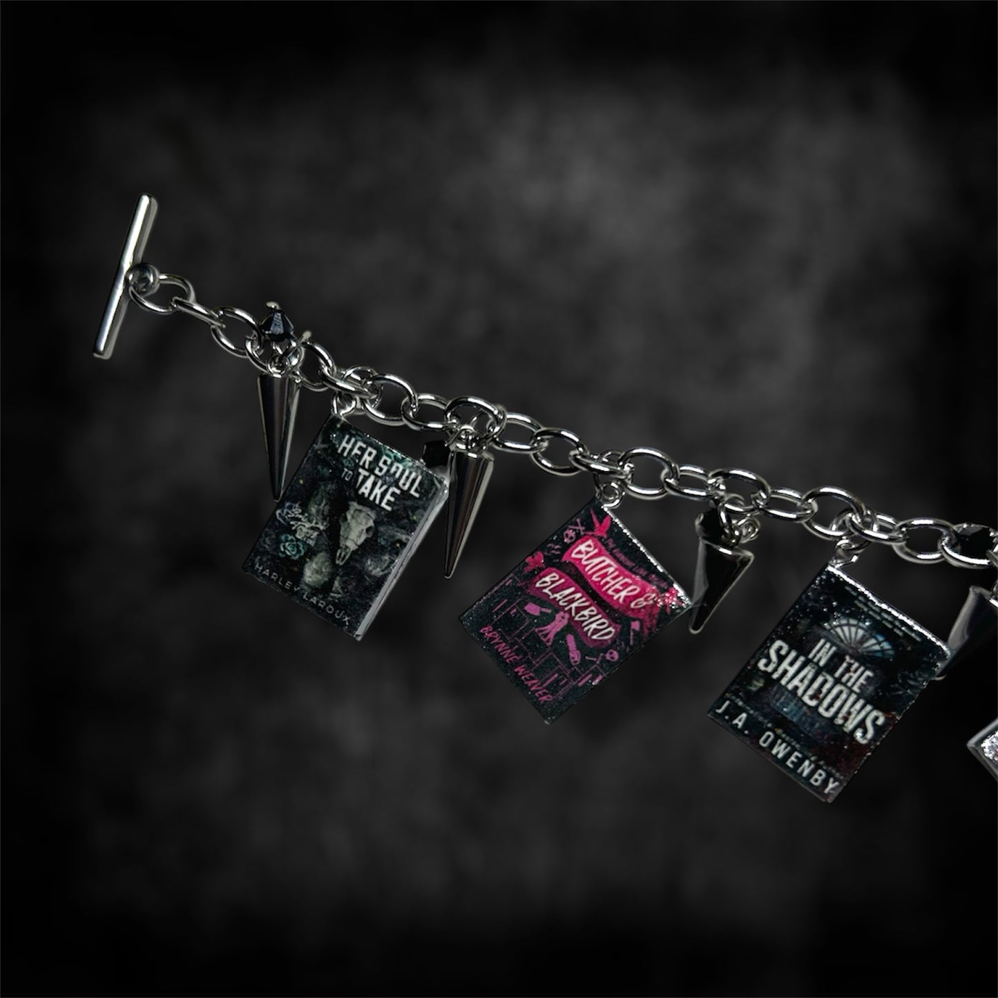 Closeup of miniature smut book charm bracelet on a blurred black distressed background