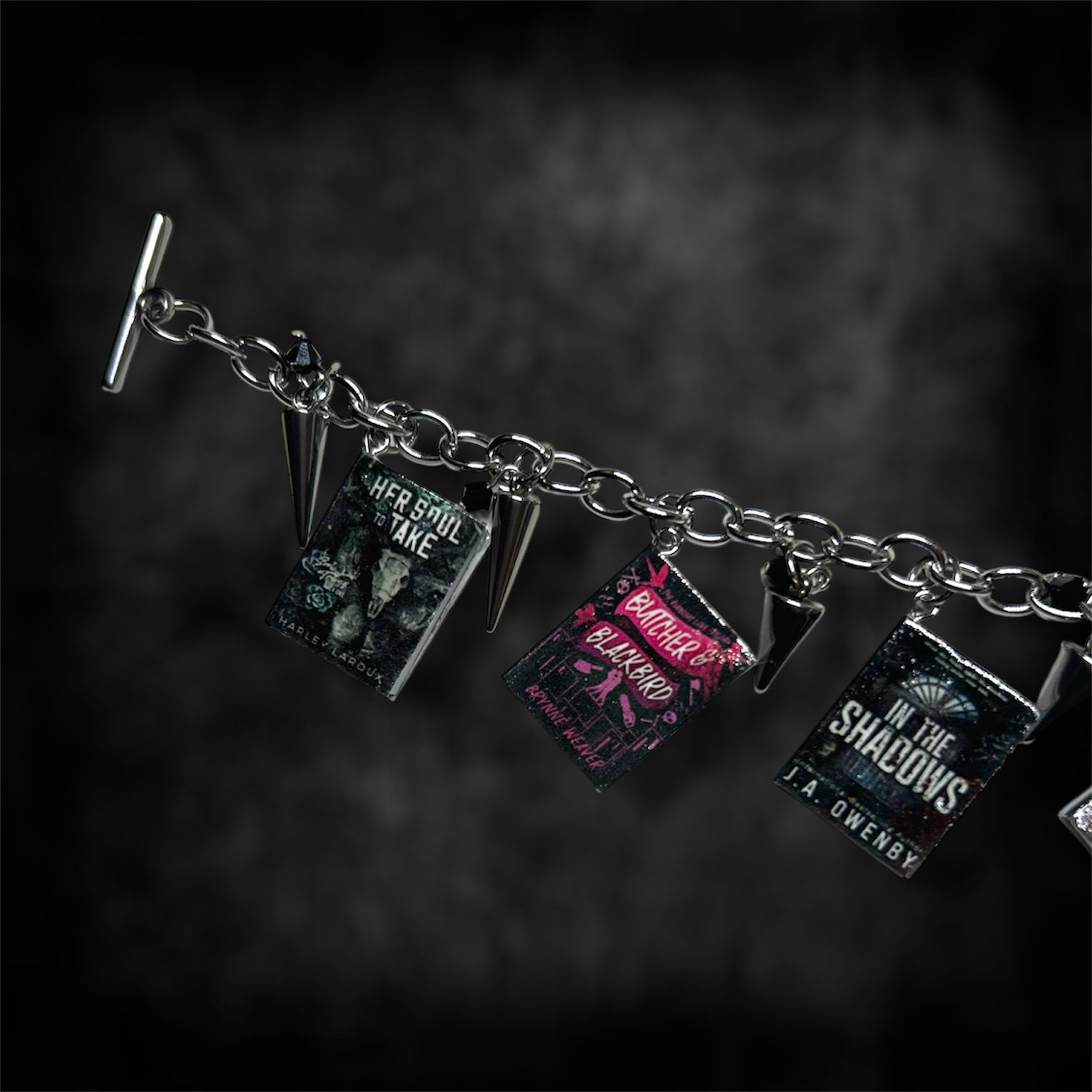 Closeup of miniature smut book charm bracelet on a blurred black distressed background