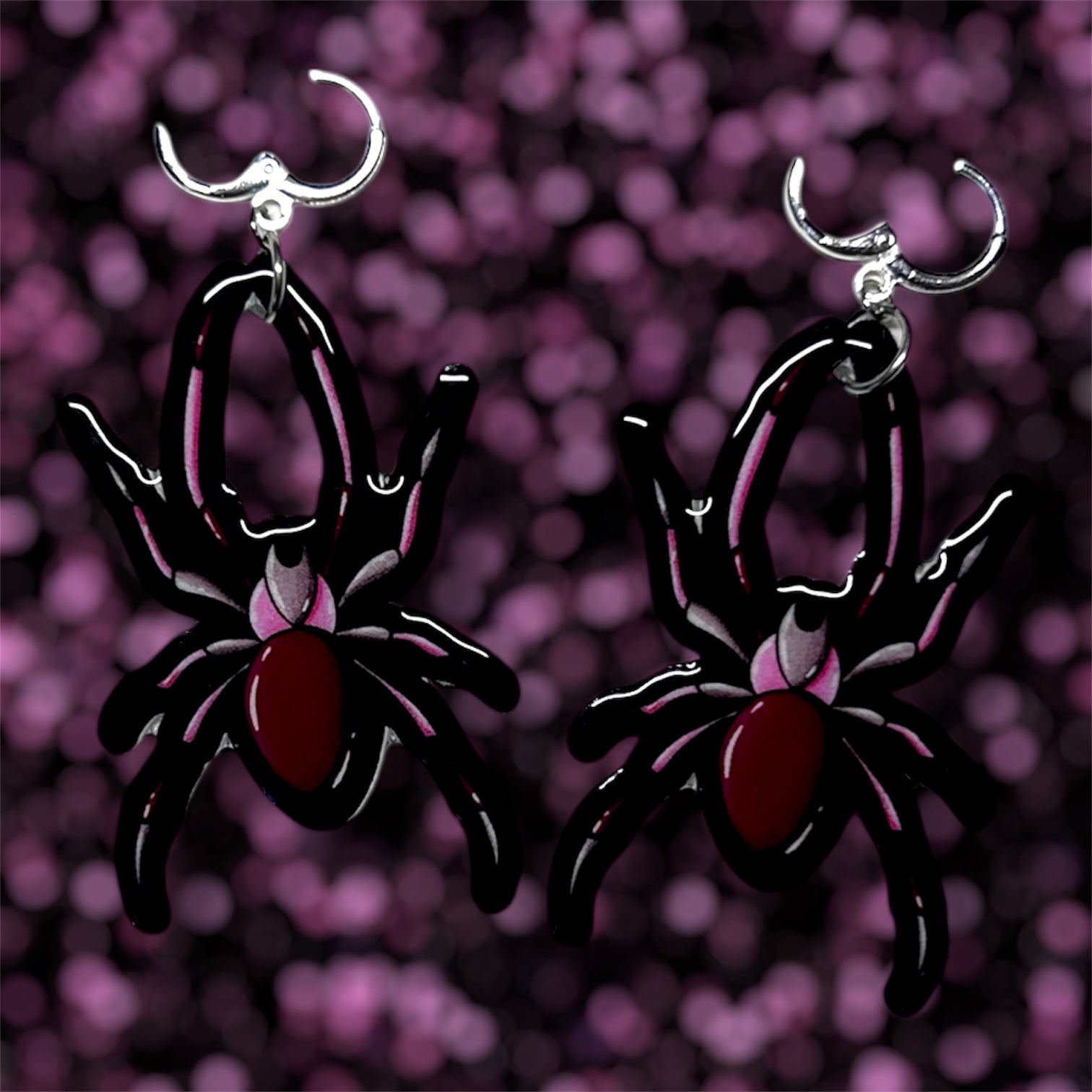 A pair of black and pink spider dangle earrings on a blurred purple and black background