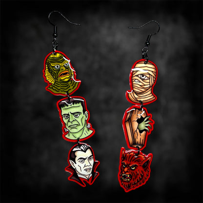 A pair of Universal Monsters stacked dangle earrings on a blurred black distressed background